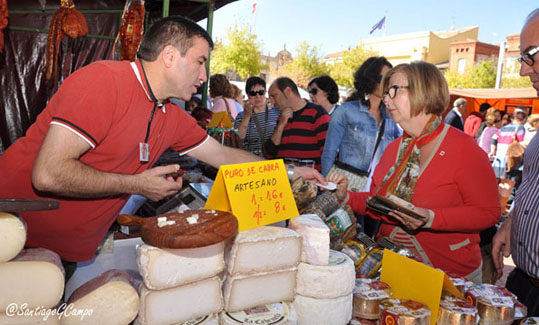 Un artesano alimentario ofrece sus quesos a una clienta en la Feria de Productos de la Tierra.